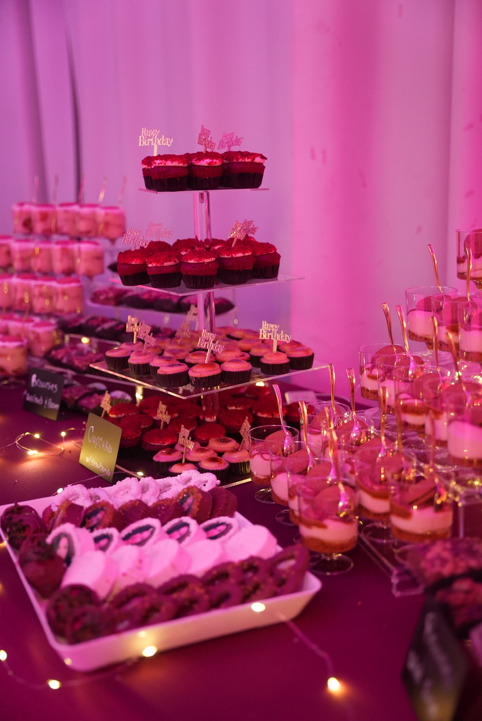 Birthday dessert table with cupcakes, sweets in glasses, and glowing lights
